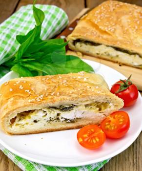 Roll layered with spinach and cheese, tomatoes in a dish on a napkin on the background of wooden boards