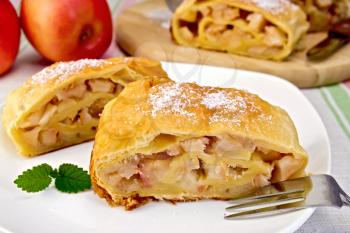 Strudel with apples and fork on the plate, apples, a knife, against a linen tablecloth