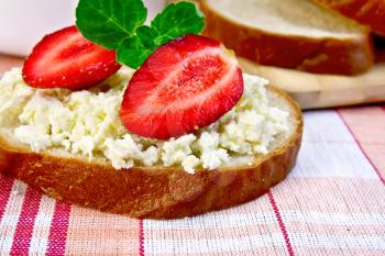 A loaf of bread with curd cream, mint and strawberries, a bowl of cottage cheese, bread on a board on a background of red checkered tablecloth