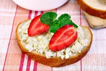 A loaf of bread with curd cream, mint and strawberries, a bowl of cottage cheese, bread on a board on a background of red checkered tablecloth