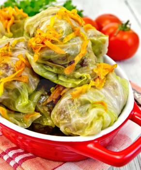 Stuffed cabbage meat in cabbage leaves with roasted carrots in a roasting pan on a red napkin, tomatoes on a lighter background board