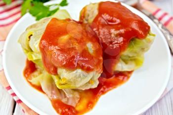 Stuffed cabbage meat in cabbage leaves with tomato sauce in a bowl on a napkin, tomatoes, parsley on a wooden boards background