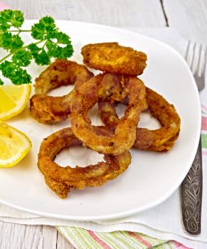 Crispy fried calamari rings on a plate with slices of lemon and parsley on a napkin on the background of wooden boards
