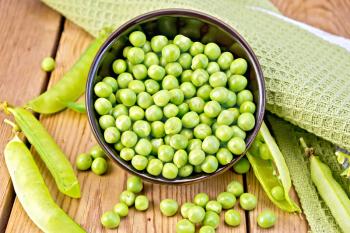 Green peas in a brown bowl, napkin, pea pods on the background of wooden boards