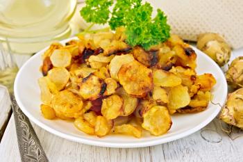 Jerusalem artichokes fried in a dish, fresh tubers, napkin, parsley, vegetable oil on a background of white wooden plank