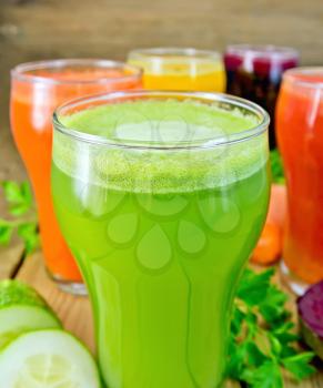 Five tall glassfuls with juice of carrot, cucumber, beetroot, tomato and pumpkin, vegetables, parsley on a wooden boards background