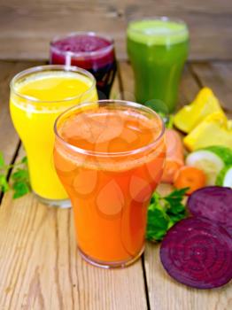 Four tall glass juice from carrot, cucumber, beetroot and pumpkin, vegetables on background of wooden boards