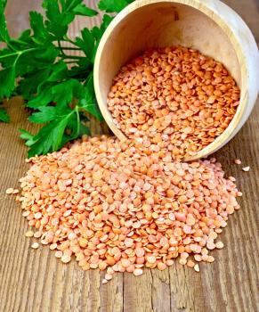 Red lentils in a wooden bowl with green parsley on a wooden boards background