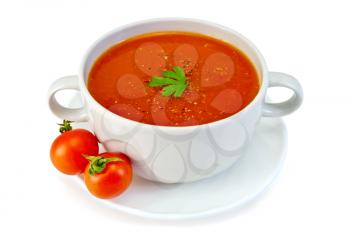 Tomato soup in a white bowl with parsley on a plate with tomatoes isolated on white background