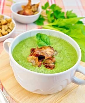 Green soup puree in a white bowl with grilled meat and spinach leaves on a wooden board on the background fabric