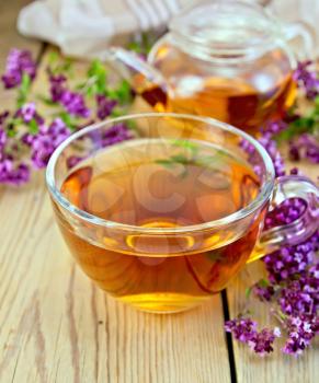 Herbal tea in a glass cup, fresh flowers, oregano, glass teapot, napkin on a wooden boards background