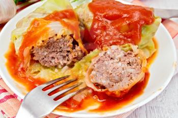 Stuffed cabbage meat in cabbage leaves with tomato sauce and a fork on a plate on a napkin, tomatoes, garlic on a background of pale wooden plank