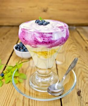 Dessert milk with blueberry, cornflakes, curd, spoon in a glassware on a wooden boards background