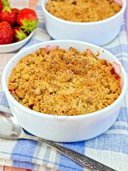 Strawberry crumble in a white bowl with a spoon on blue napkin, strawberries on linen tablecloth background