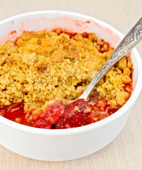 Strawberry crumble in a white bowl with a spoon on a linen fabric background
