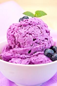 Blueberry ice cream with mint and berries in a bowl on a background of purple cloth and wooden planks
