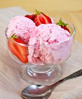 Strawberry ice cream in a glass bowl with strawberries, spoon on a napkin on a wooden boards backgrou