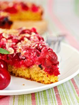 A piece of sweet cake with cherries on a plate against the background of a linen tablecloth