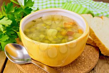 Soup of green peas in a yellow cup, napkin, bread, spoon, parsley on a wooden boards background