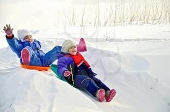 Two little girls on a sled sliding down a hill on snow in winter