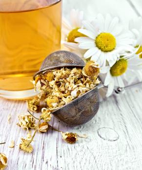Dried chamomile in strainer, cup with herbal tea on a background of light wooden boards