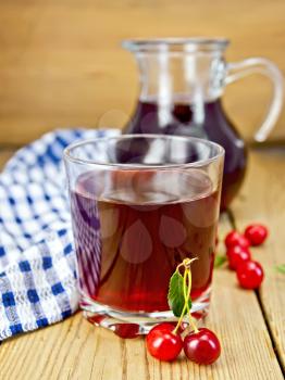 Cherry compote in a glass and pitcher, napkin on a wooden boards background