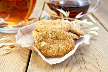 Oatmeal cookies with a stalk of oats on the paper, a cup of tea and teapot wooden boards background