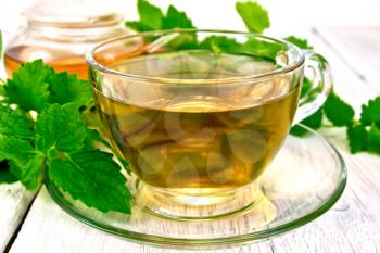 Herbal tea melissa in a glass cup and teapot, fresh melissa leaves on the background light wooden boards