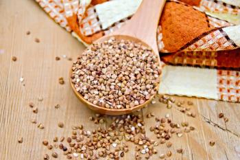 Buckwheat in a spoon, brown checkered doily on a wooden boards background