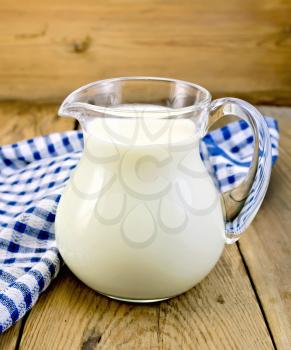 Milk in a glass jar with a blue checkered cloth on a wooden boards background