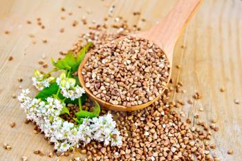 Buckwheat in a spoon with white flower buckwheat on a wooden boards background