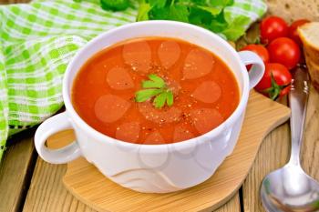 Tomato soup in a white bowl, green napkin, spoon, tomato, parsley, bread on a wooden boards background