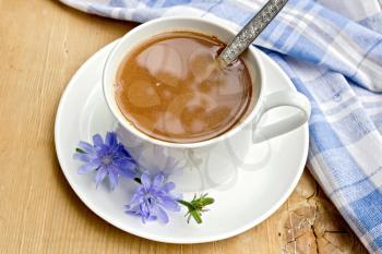 Chicory drink in a white cup with a flower and a spoon, napkin on a wooden boards background