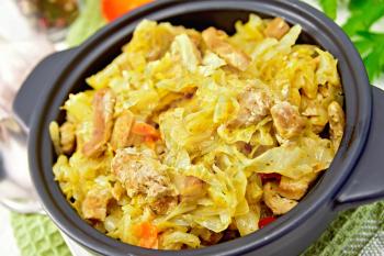 Cabbage stew with meat black in a roasting pan with lid, napkin, pepper, parsley. spoon on a light background boards