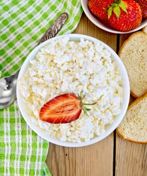 Cottage cheese in a white bowl with strawberries and mint, spoon, napkin, bread on a wooden boards background