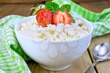 Cottage cheese in a white bowl with strawberries and mint, spoon, green cloth on a wooden boards background