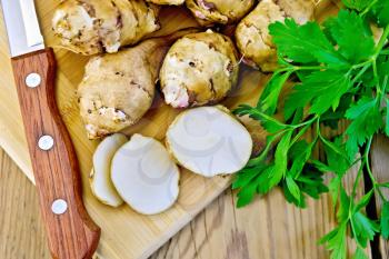 One cut and a few whole tubers of Jerusalem artichoke with parsley, knife on a wooden board