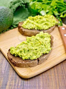 Two slices of rye bread with guakomole, avocado, napkin, parsley against the dark wooden board