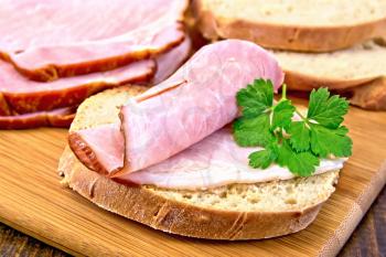 Bread with a slice of smoked ham and a sprig of parsley on a wooden boards background