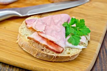 Bread with a slice of smoked ham and a sprig of parsley, knife on a wooden boards background