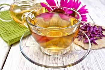 Herbal tea in a glass cup, teapot, fresh and dried flowers of Echinacea, napkin on a wooden boards background