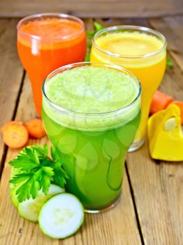 Three tall glass of carrot juice, cucumber and pumpkin with vegetables and parsley on a wooden boards background