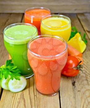 Four tall glass of tomato juice, carrot, cucumber and pumpkin, vegetables, parsley on a wooden boards background