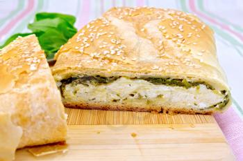 Roll layered with spinach and cheese on a wooden board, spinach leaves on a background of a linen tablecloth