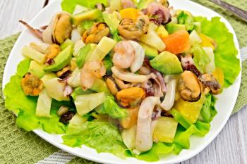 Salad with shrimps, octopus, mussels and calamari with avocado, lettuce, pineapple in plate on a napkin, fork on the background light wooden boards