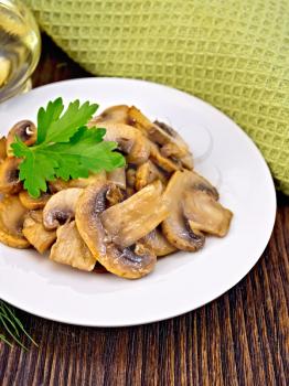 Champignons fried in a plate with a leaf of parsley, oil in carafe, napkin on a wooden boards background