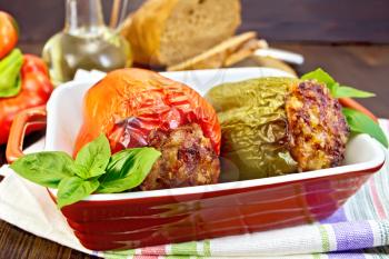 Two sweet peppers stuffed with meat and rice with basil leaves in a brown roasting pan on a napkin on a wooden boards background