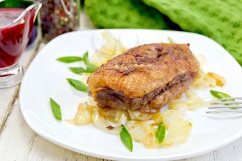 Whole roasted duck breast with stewed cabbage and green onions in a white plate, plum sauce, a towel on the background light wooden boards