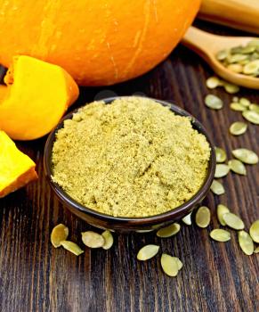 Pumpkin flour in a bowl, peeled pumpkin seeds in a spoon on the table, slices of fresh pumpkin on a dark wooden board