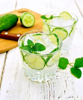 Lemonade with cucumber and mint in two glasses, a knife, a cucumber on a wooden boards background